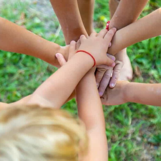 a group of children stand together putting their hands in to play a game - team spirit concept